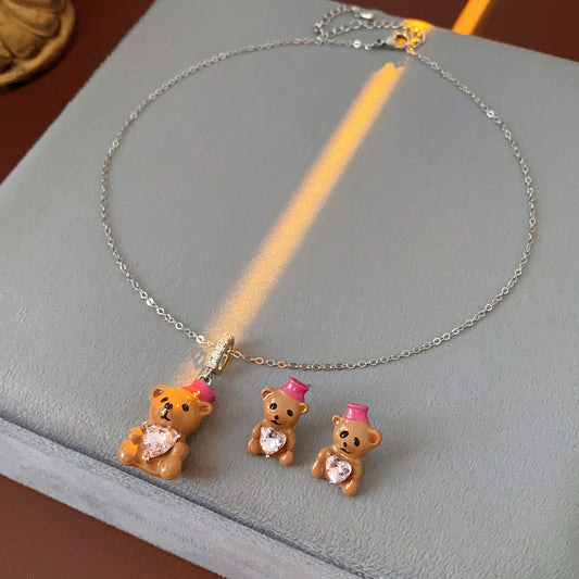 Silver-tone necklace with coffee teddy pendant and pink hat, matching teddy stud earrings with heart crystal — Sweetheart Teddy Crystal Jewelry.