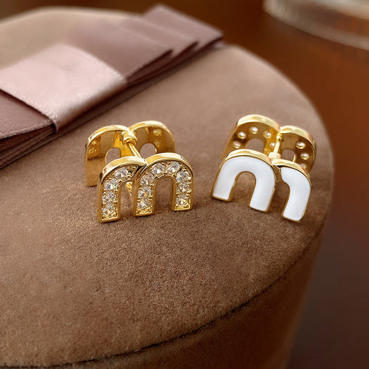 Gold arc “M” stud earrings in pavé crystal and white enamel — Muse Arc Pavé Stud Earrings.