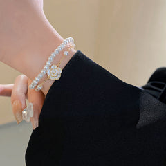 Layered faux-pearl bracelet with gold-tone chain and white enamel flower charm placed in a green jewelry tray — Petite Pearl Bloom Layered Bracelet.