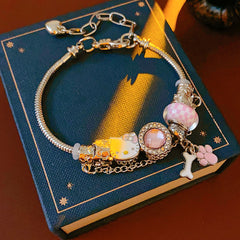 Rosy Pawprints Charm Bracelet — silver-tone snake chain with pink crystal bezel, checker enamel bead, cat-with-bow, paw and bone charms in jewelry tray