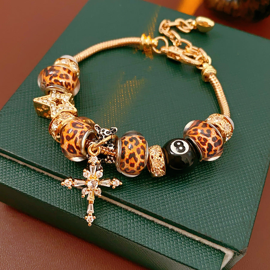Leopard Cross Luxe Bracelet with leopard-patterned beads, zircon accents, black 8-ball bead, and cross pendant on gold chain