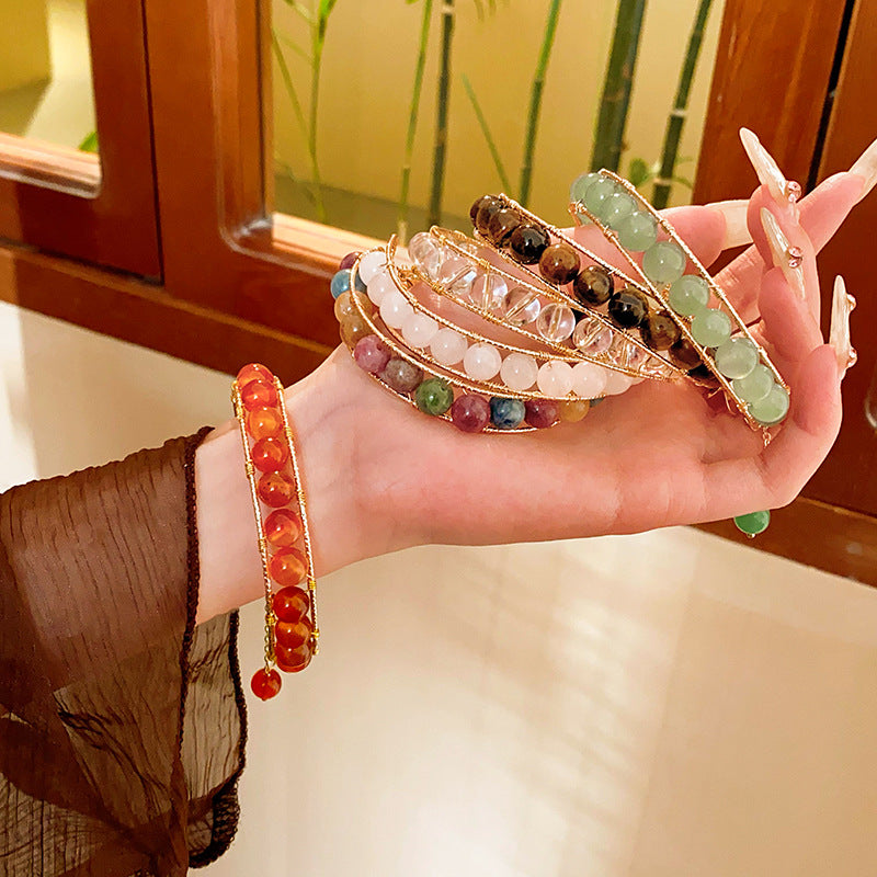 Natural stone beaded bracelets in multiple colors including red agate, rose quartz, and white crystal, with golden accents displayed in a jewelry tray.