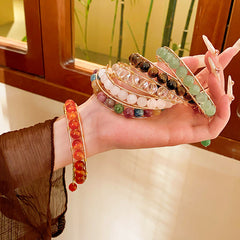 Natural stone beaded bracelets in multiple colors including red agate, rose quartz, and white crystal, with golden accents displayed in a jewelry tray.