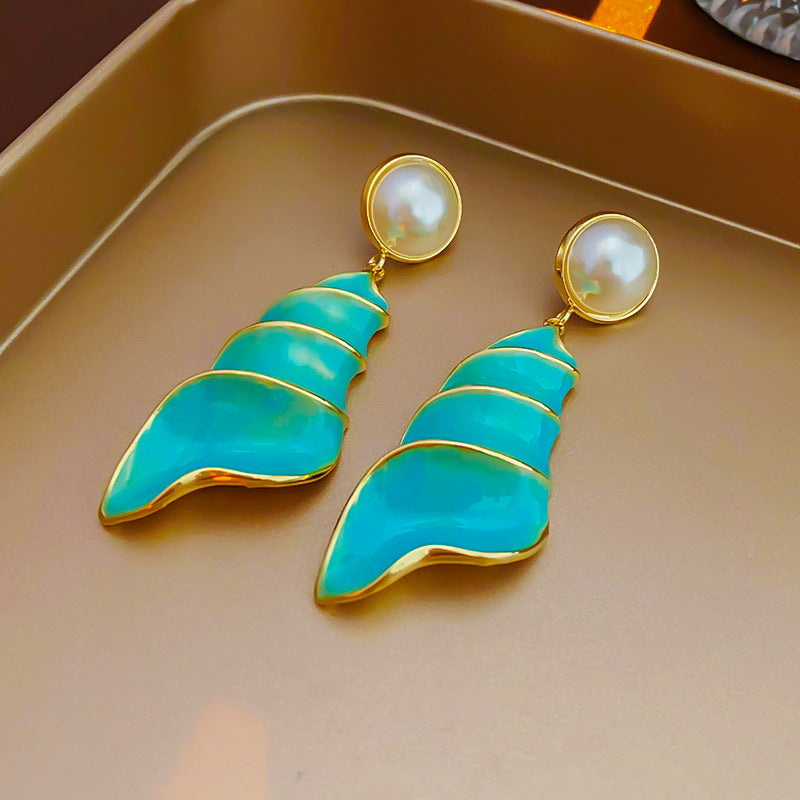 Lagoon Spiral Pearl Drop Earrings — glossy turquoise spiral shell drops with pearl studs and gold trim on jewelry tray