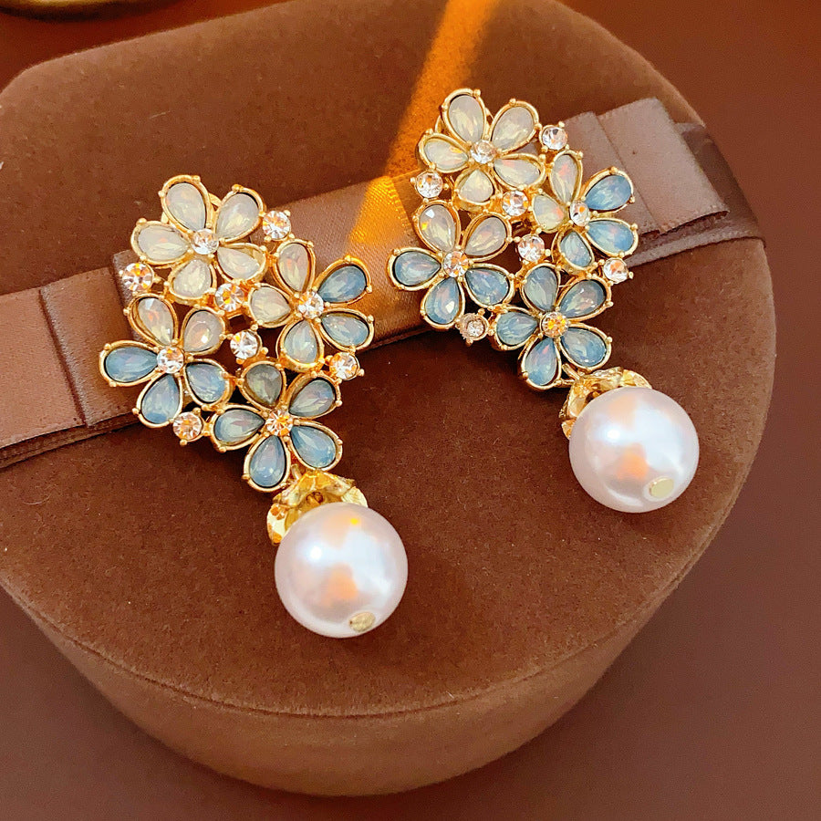 Gold floral cluster earrings with ice-blue petals, crystal accents, and a single luminous faux-pearl drop — Ethereal Petal Pearl Earrings.