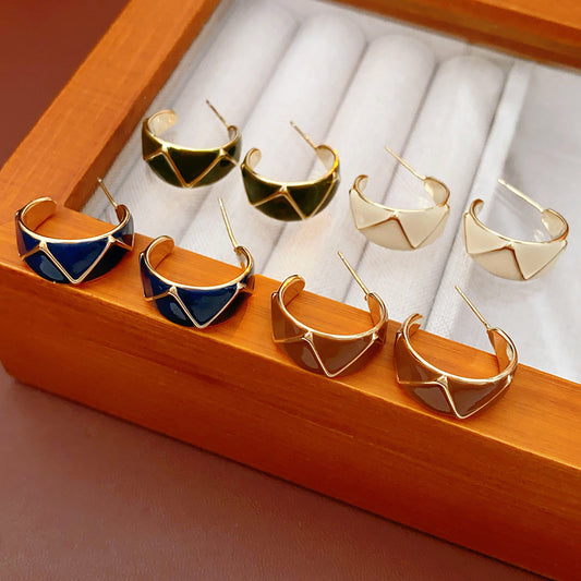 Set of four geometric enamel hoop earrings in white, blue, coffee, and green displayed in a jewelry tray