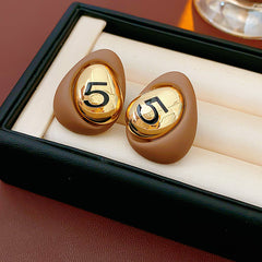 Matte pebble stud earrings with mirrored gold dome engraved with 5 — in white, black, coffee, and red — Gilded Numeral 5 Pebble Studs.