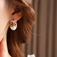 Enamel masquerade face stud earrings with red and black halves and gold filigree on a velvet jewelry box — Venetian Masquerade Studs.