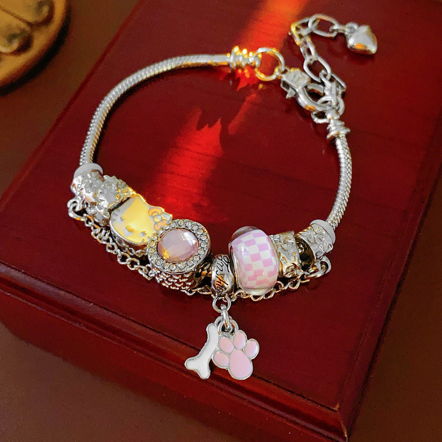 Rosy Pawprints Charm Bracelet — silver-tone snake chain with pink crystal bezel, checker enamel bead, cat-with-bow, paw and bone charms in jewelry tray