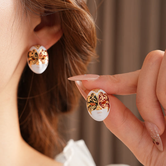 Enamel masquerade face stud earrings with red and black halves and gold filigree on a velvet jewelry box — Venetian Masquerade Studs.