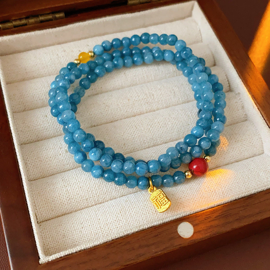 Blue multi-wrap beaded bracelet with red accent bead and gold charm — Azure Charm Wrap Bracelet.