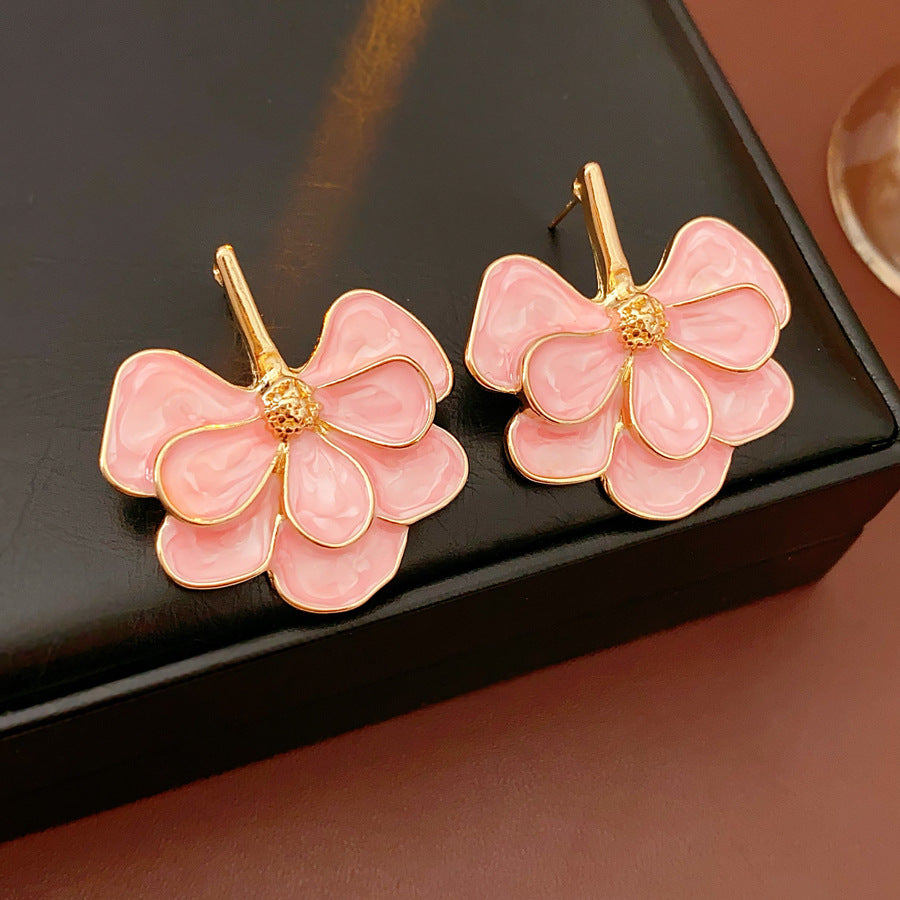 Close-up of pink enamel flower earrings with gold tone petals, statement design on jewelry tray
