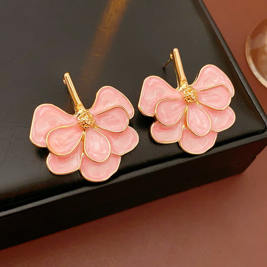 Close-up of pink enamel flower earrings with gold tone petals, statement design on jewelry tray
