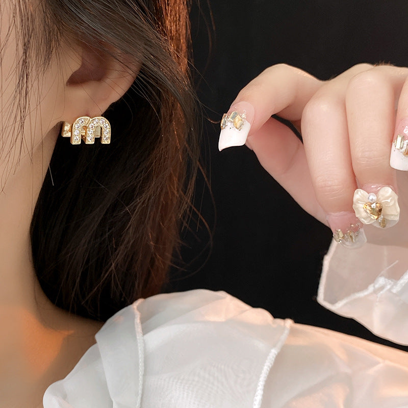 Gold arc “M” stud earrings in pavé crystal and white enamel — Muse Arc Pavé Stud Earrings.