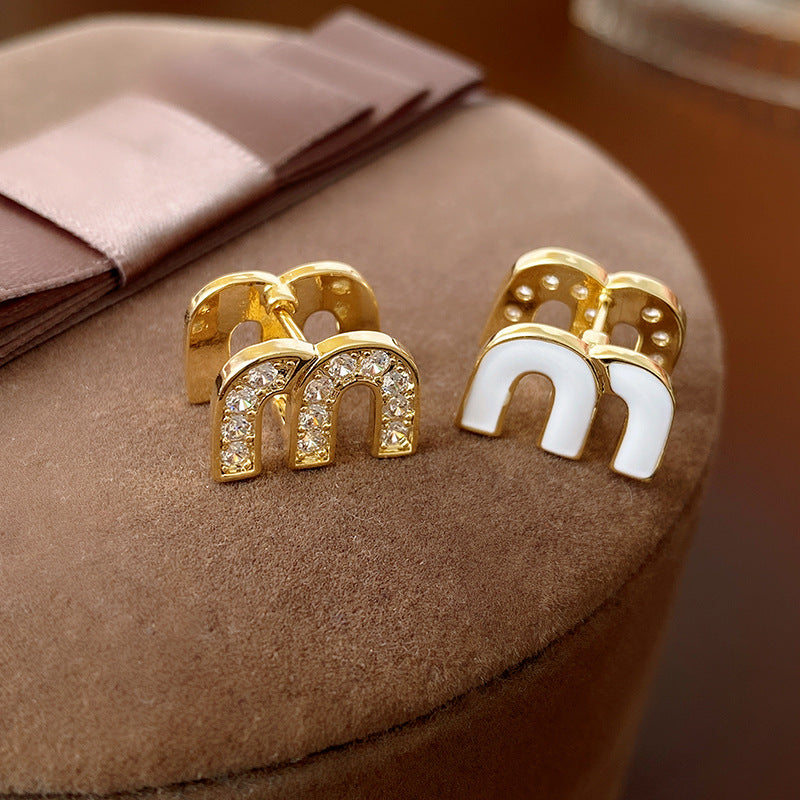 Gold arc “M” stud earrings in pavé crystal and white enamel — Muse Arc Pavé Stud Earrings.