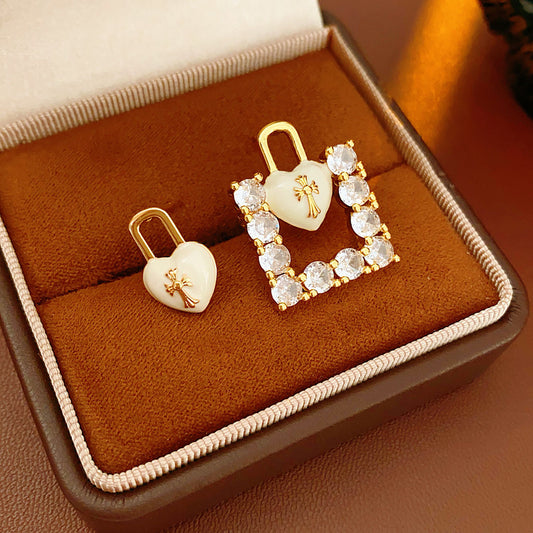 Enamel heart-lock and rhinestone square padlock mismatched stud earrings in gold tone.
