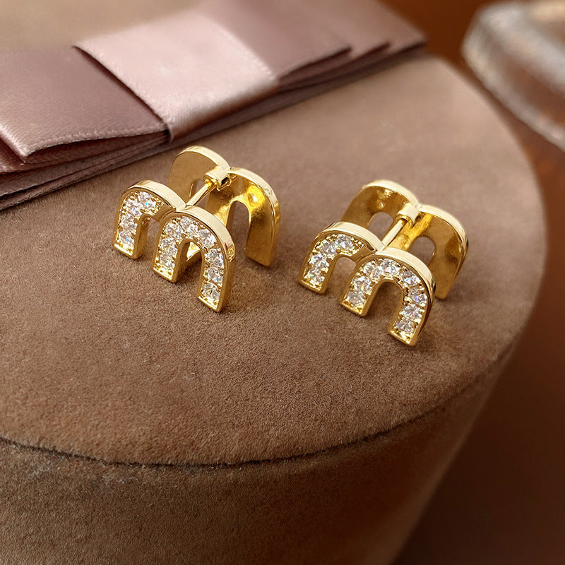 Gold arc “M” stud earrings in pavé crystal and white enamel — Muse Arc Pavé Stud Earrings.