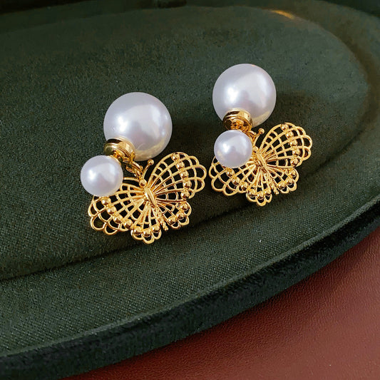 Double-pearl stud earrings with gold-tone butterfly and star charms displayed in a jewelry tray — Double Pearl Charm Studs.