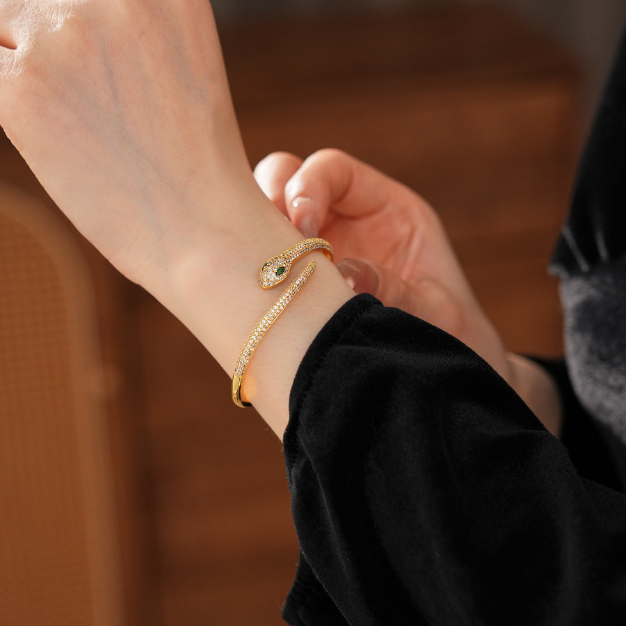 Gold and silver snake-shaped zircon bangles with emerald eyes — Serpent Luxe Bangle by Glazenya.