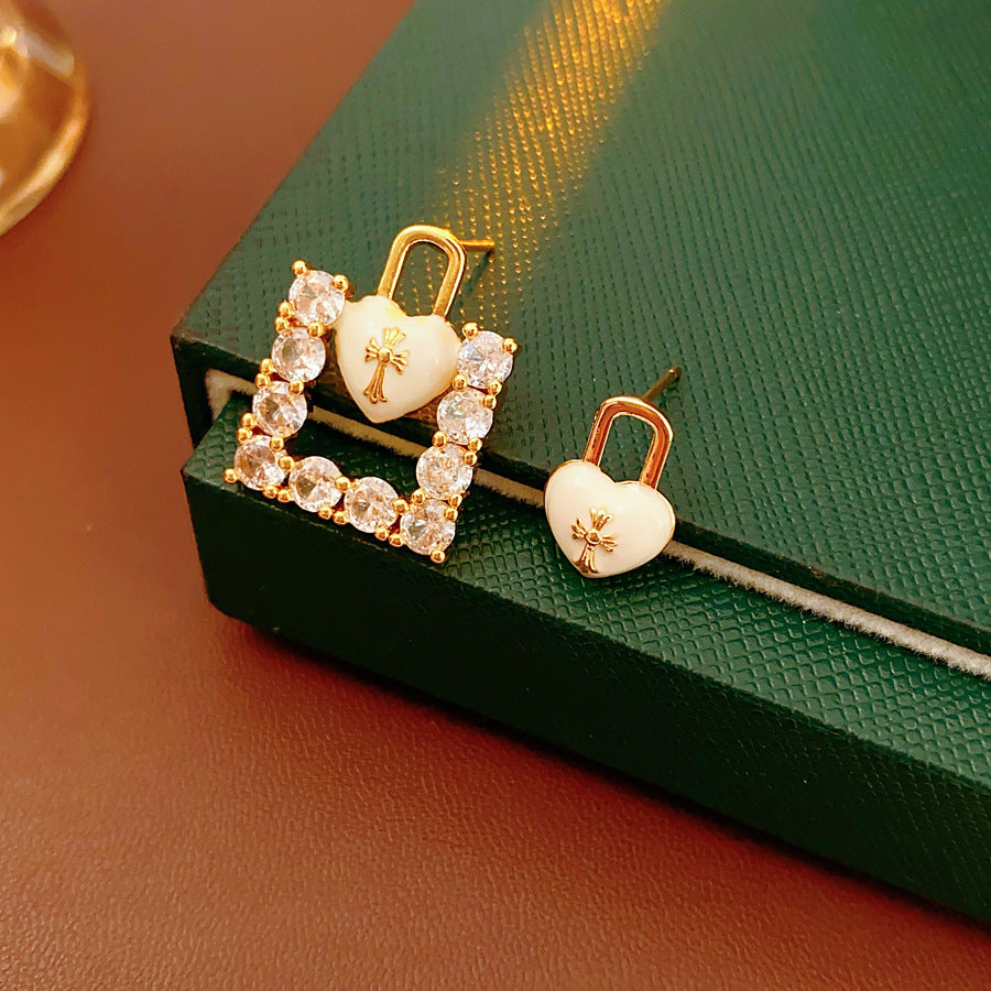 Enamel heart-lock and rhinestone square padlock mismatched stud earrings in gold tone.