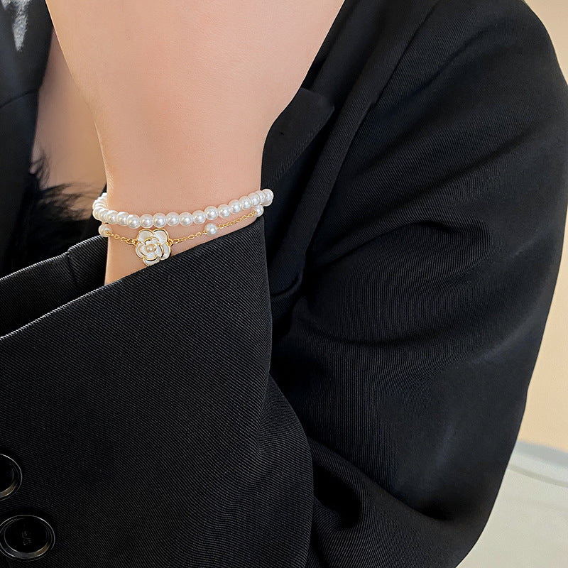 Layered faux-pearl bracelet with gold-tone chain and white enamel flower charm placed in a green jewelry tray — Petite Pearl Bloom Layered Bracelet.