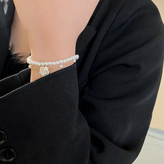 Layered faux-pearl bracelet with gold-tone chain and white enamel flower charm placed in a green jewelry tray — Petite Pearl Bloom Layered Bracelet.
