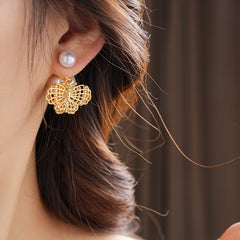 Double-pearl stud earrings with gold-tone butterfly and star charms displayed in a jewelry tray — Double Pearl Charm Studs.
